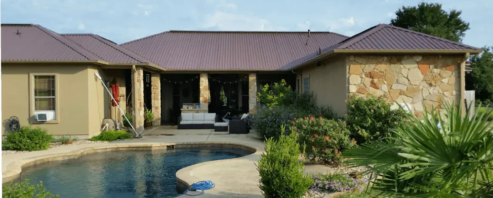 Backyard with a pool and the backside of a rock house with a tile roof
