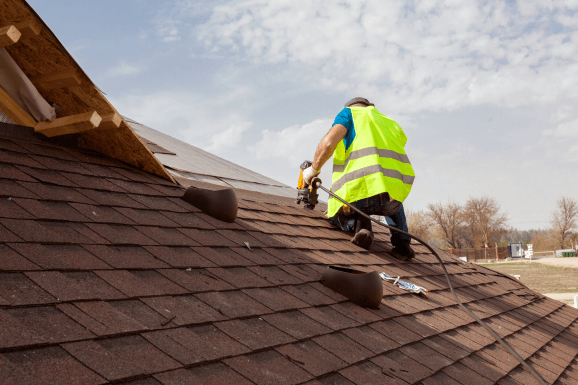 An employee attaching shingles on top of a roof